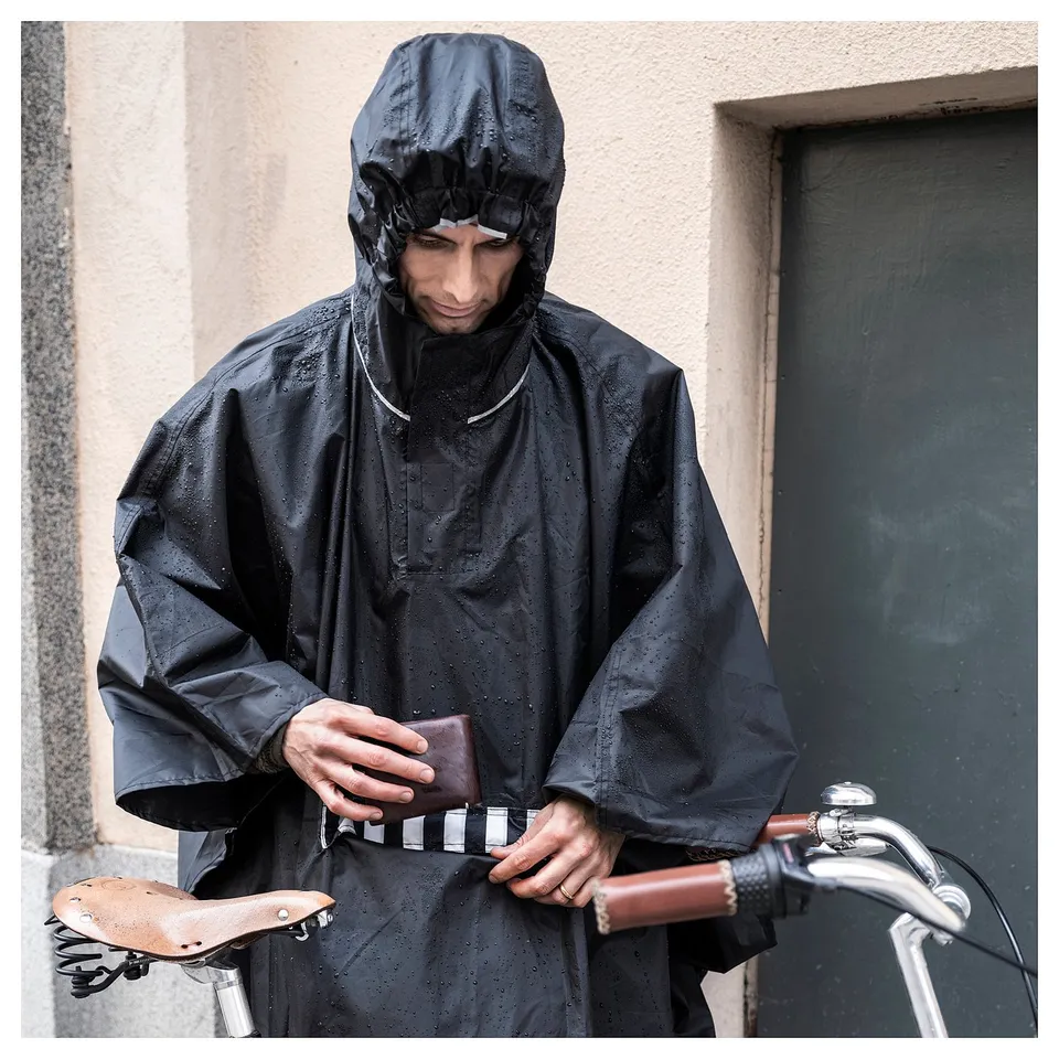 Person in black rain poncho, holding wallet, standing next to bike.