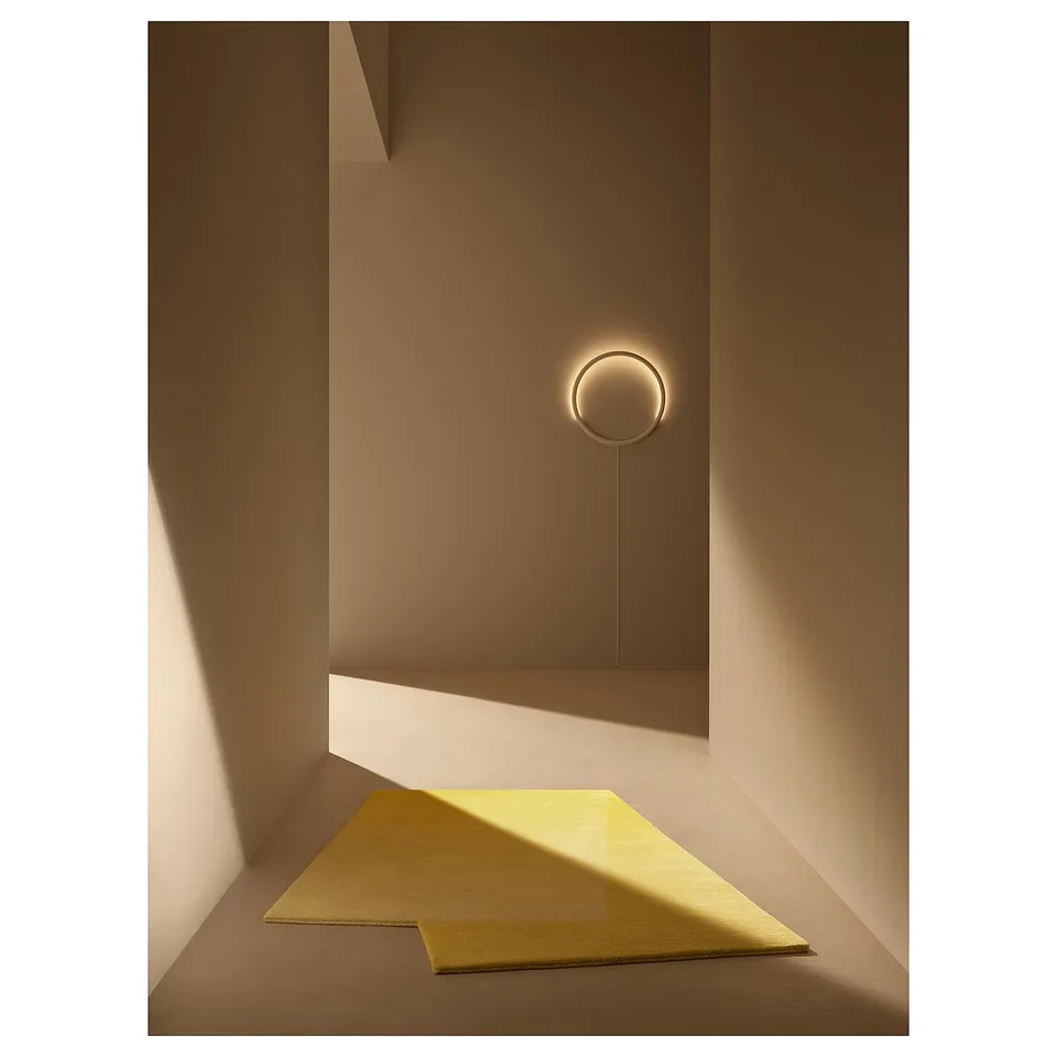 Modern, minimalist wall lamp in gold, emitting soft glow, mounted on beige wall.
