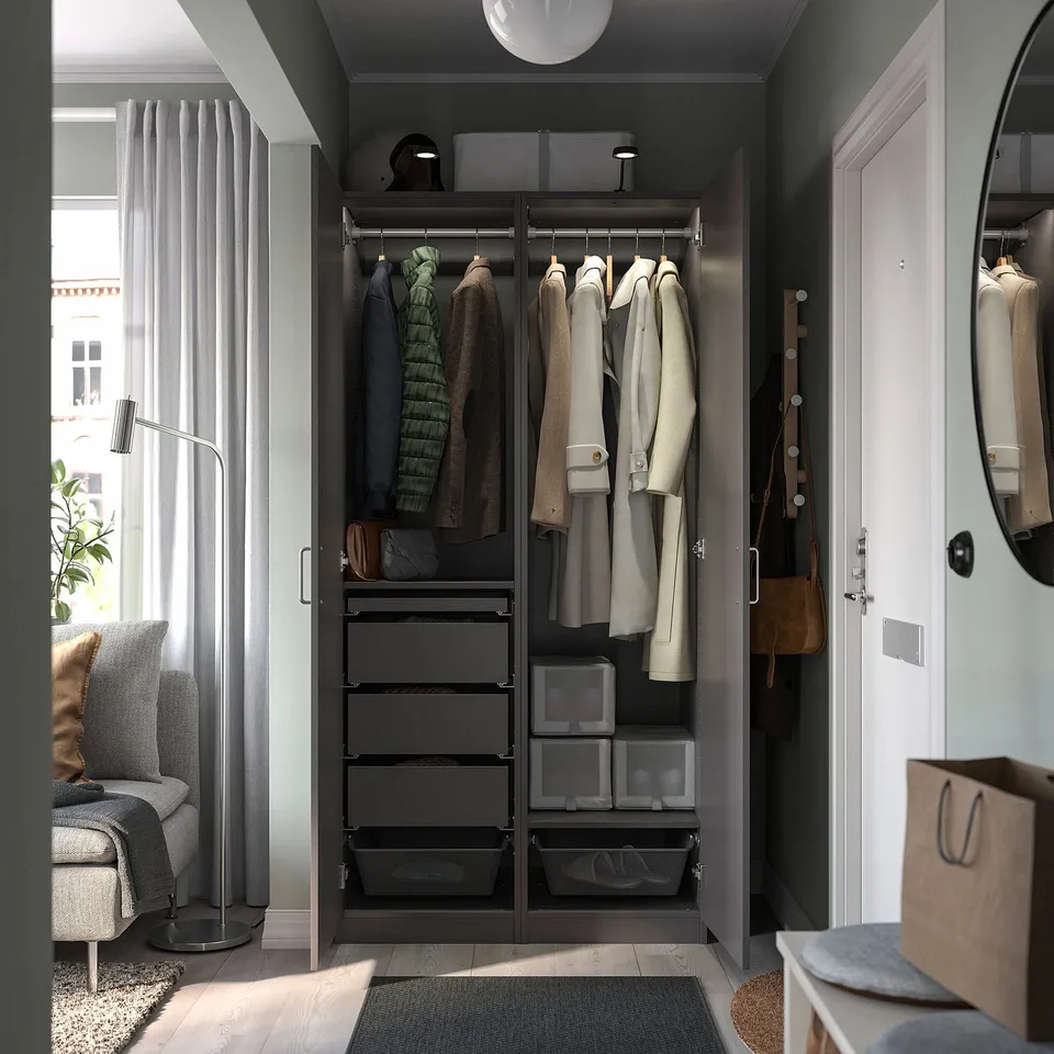 A modern, dark-colored PAX wardrobe with hangers and storage drawers. It has a sleek design and organised clothing items.