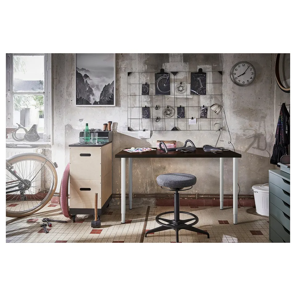 Office desk setup with wooden top, metal legs, hanging art, cycle, and tools.