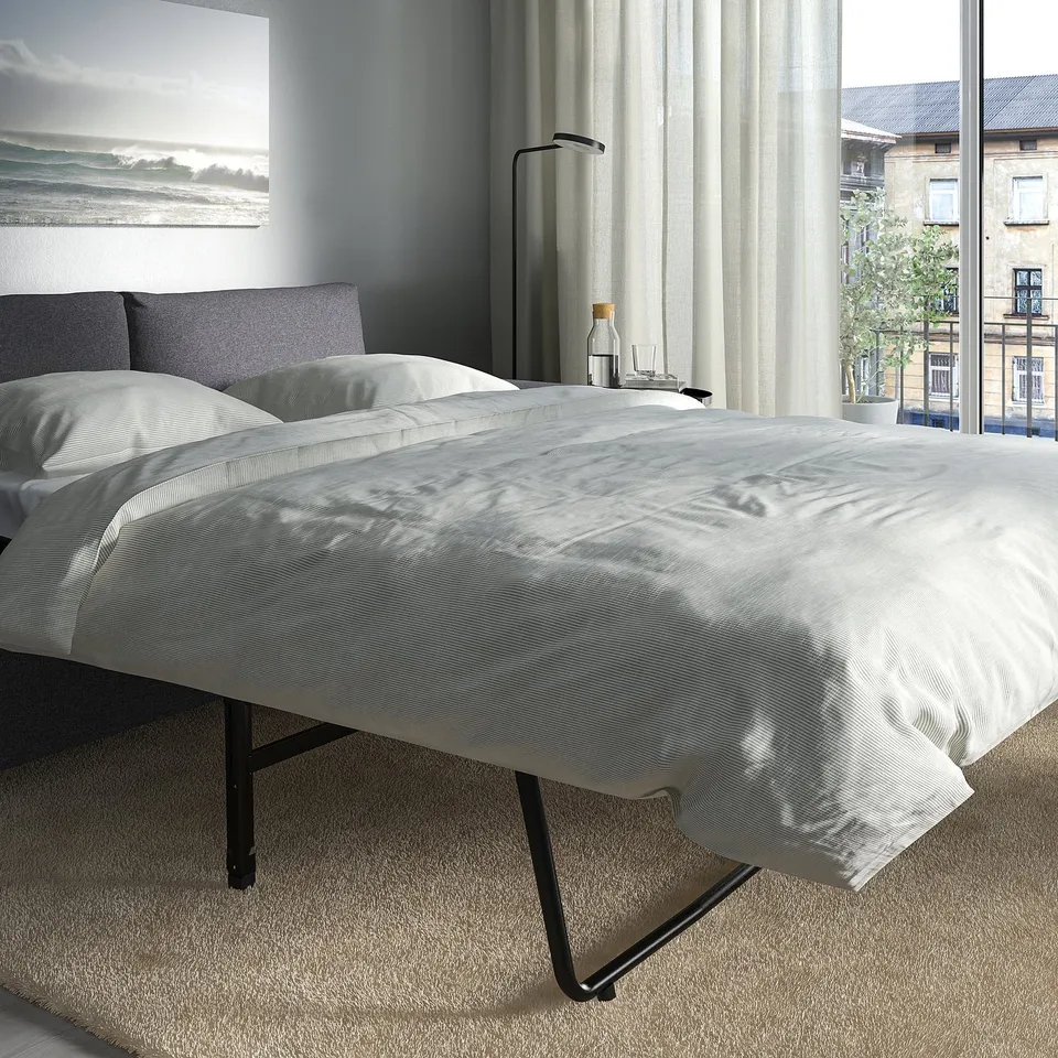 Modern bedroom with VIMLE sofa-bed, neatly made mattress, side table, and city view.