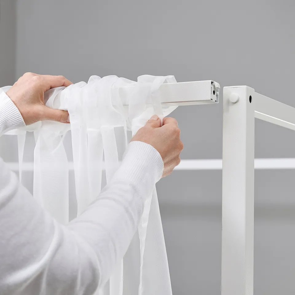 Person adjusting white curtains on a VITARNA four-poster bed frame.