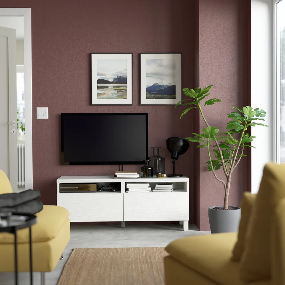 Modern living room with maroon walls, BESTÅ tv stand with electronics, yellow chairs, green plant, nature photos.
