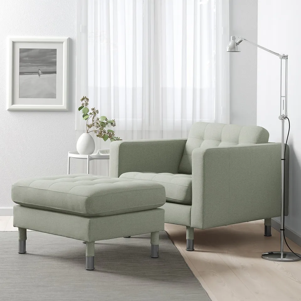 Light green LANDSKRONA chair & footstool with oak legs, tufted fabric, cosy nook setup. Side table with flowers, floor lamp.
