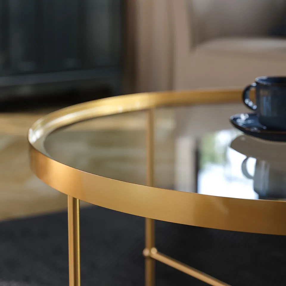Elegant gold-toned metal coffee table with glass top, featuring refined details and sturdy design.