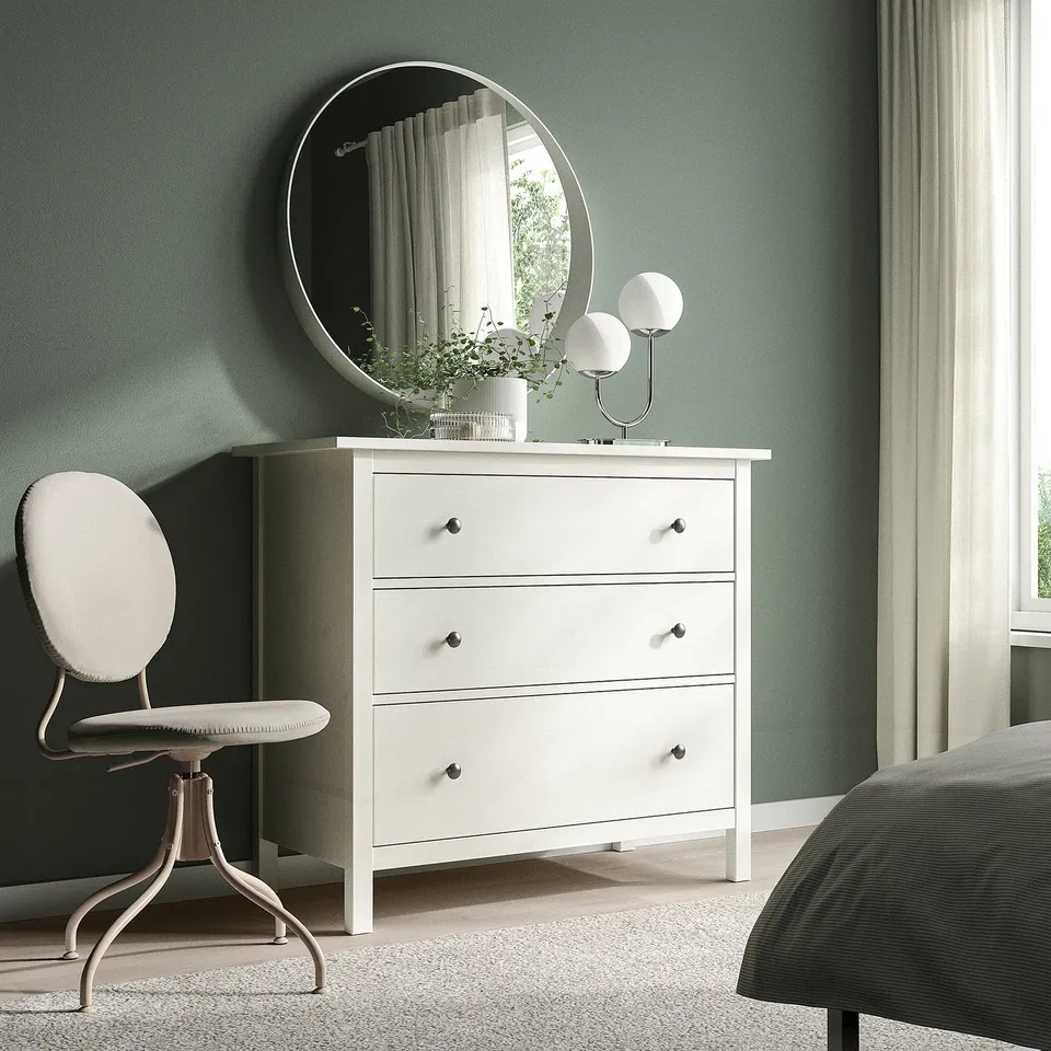Minimalist bedroom setup: white BJÖRKBERGET swivel chair, white dresser, round mirror, green wall.