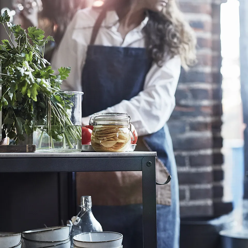 Person in blue apron in kitchen with island, bowls, jar, and vase.