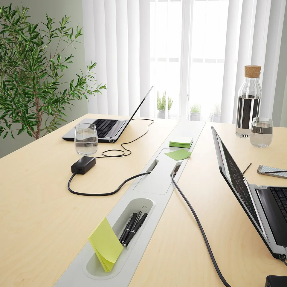 A sleek, modern conference table with integrated cable management, a footrest, and a section for pens, ideal for meetings.