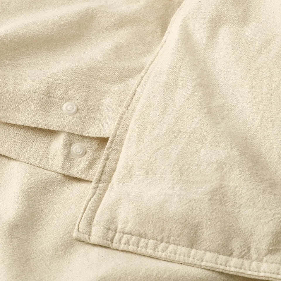 Close-up of an off-white duvet cover with unbleached edges and plastic press-stud closure on bottom.