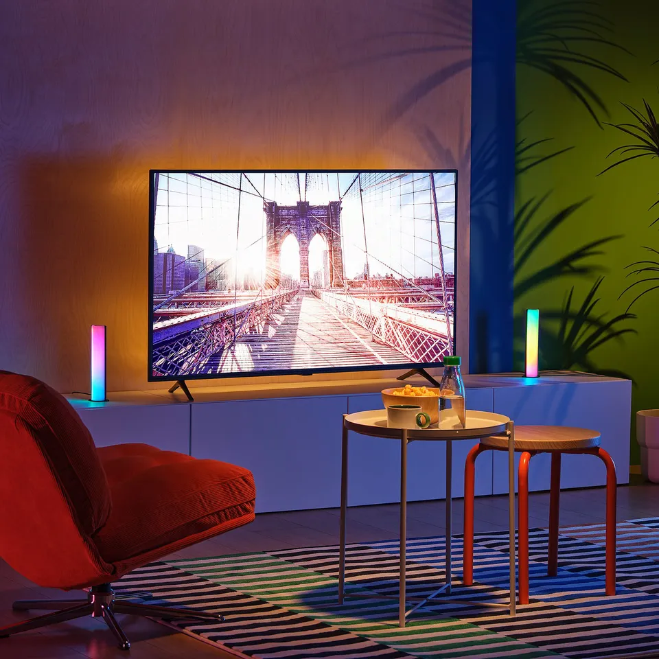 Tv displays brooklyn bridge with lights, on blue stand, red chair, snacks nearby.