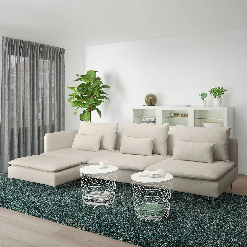 Modern cream l-shaped SÖDERHAMN sofa in bright room with side tables, green rug, and plant.