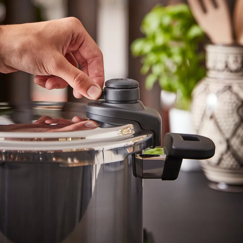 A person adjusts the pressure valve on an IKEA 365+ stainless steel pressure cooker.