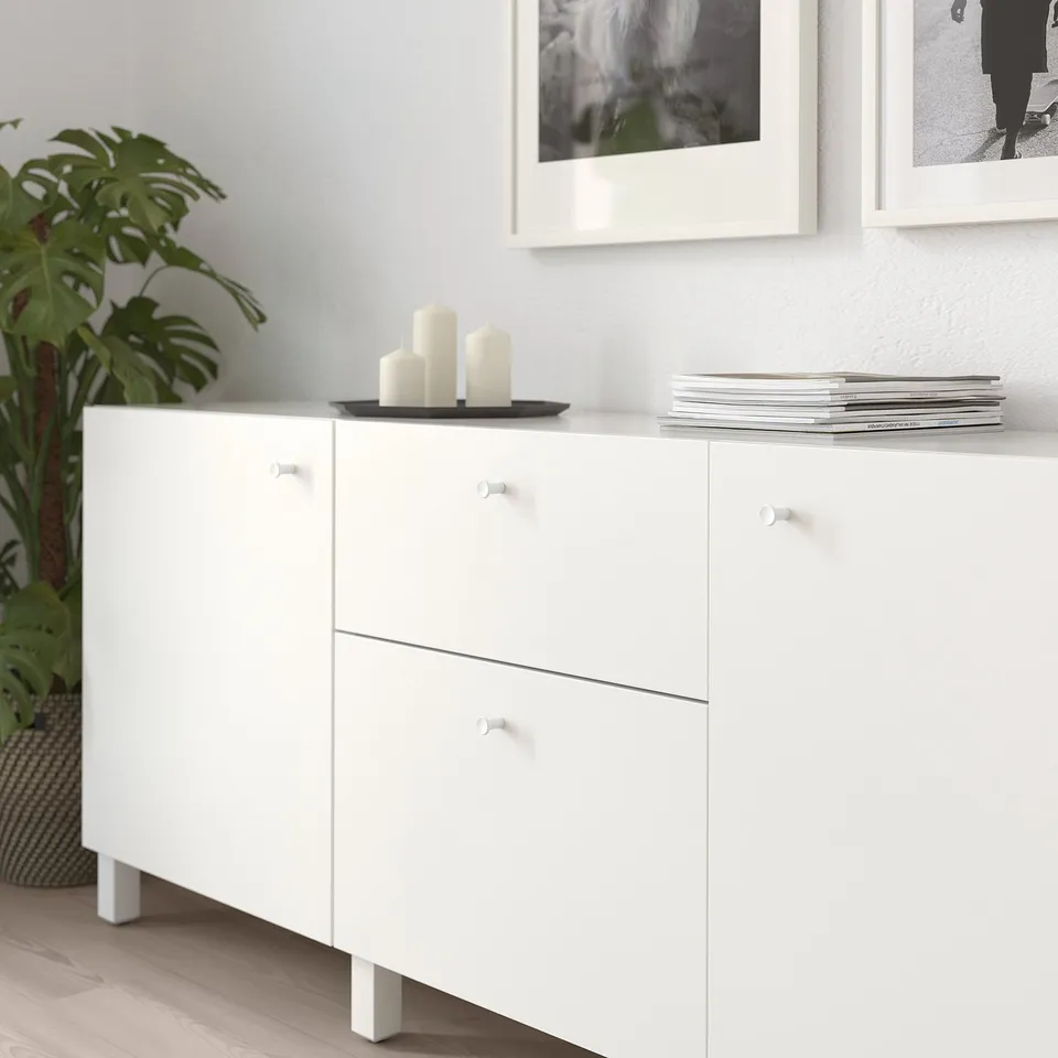 White cabinet with knobs and three candles on top, next to a plant.