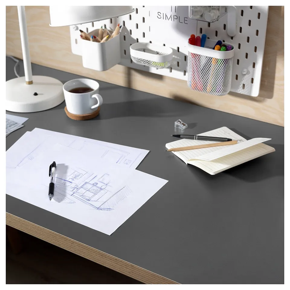 Modern desk setup with black surface, white lamp, coffee cup, papers, and organisers.