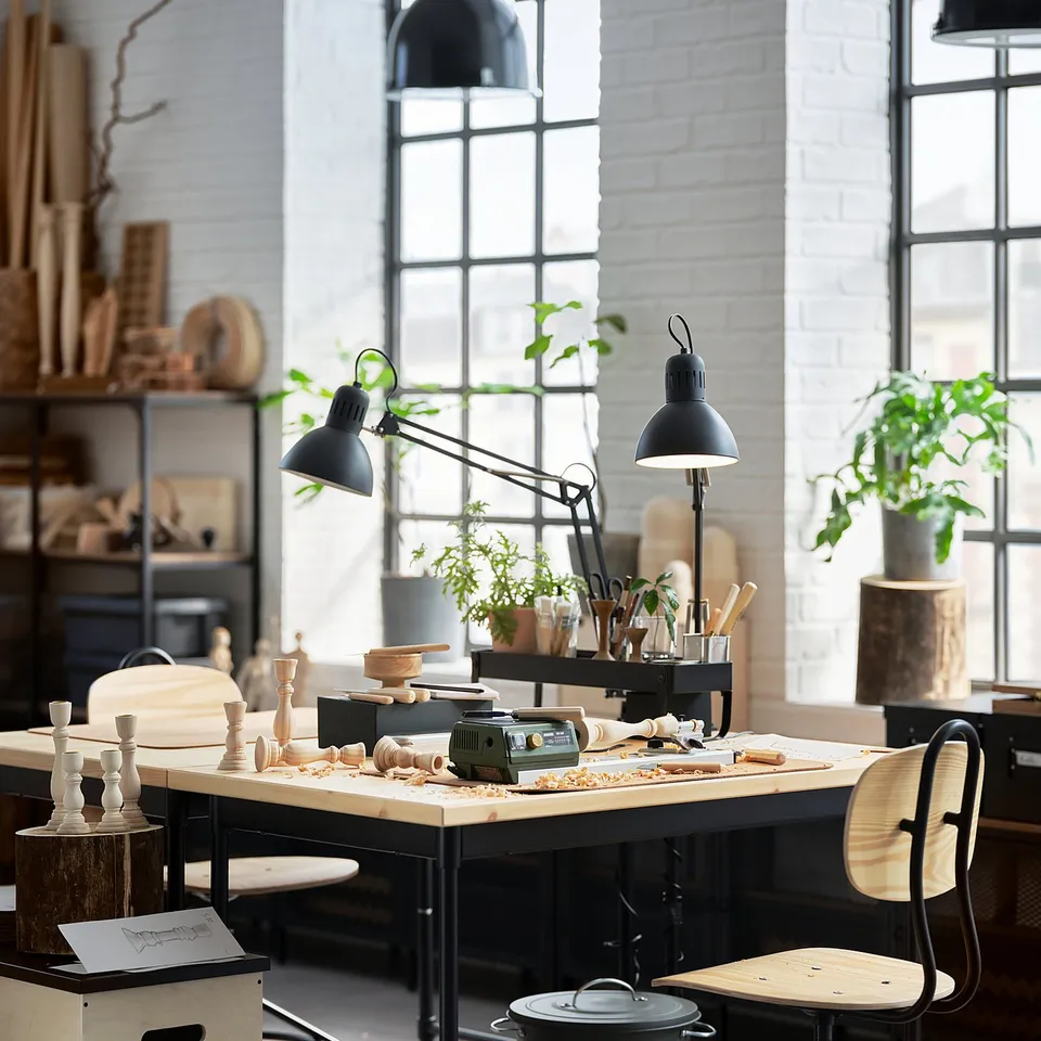 Industrial-style workspace featuring KULLABERG black metal desk with wooden top, surrounded by tools, plants, and black chairs.
