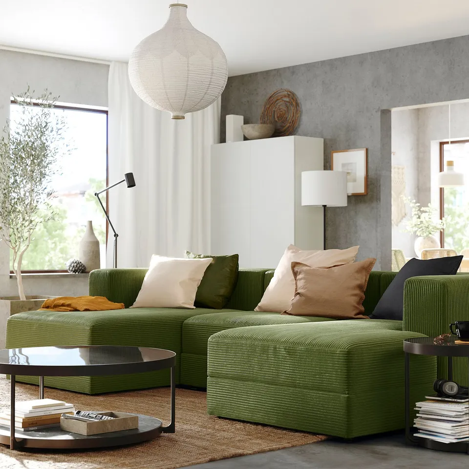 Modern living room with olive green modular JÄTTEBO sofa, ample cushions, hanging lamp, grey walls, and large windows offering natural light.