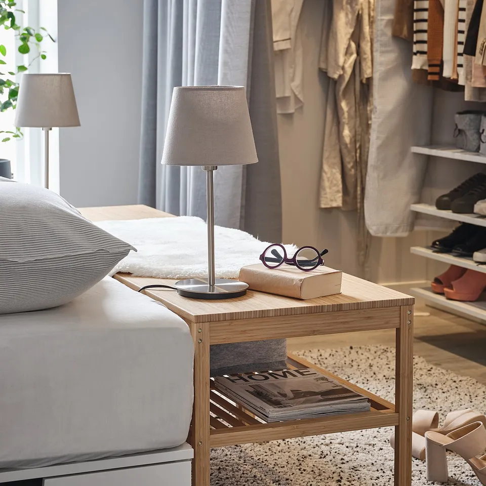 Bedside table with lamp, books, and glasses. Modern design, light wood finish.