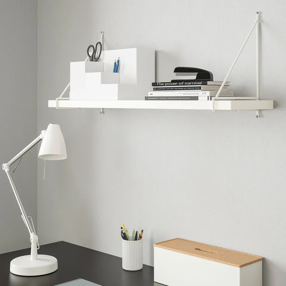 White PERSHULT wall shelf holds books & office supplies. Modern design, sturdy steel. Accompanies a small desk lamp & storage box.