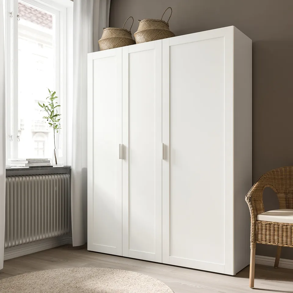 White SANNIDAL cabinet with woven baskets on top, next to a window with a tall plant beside a wicker chair.