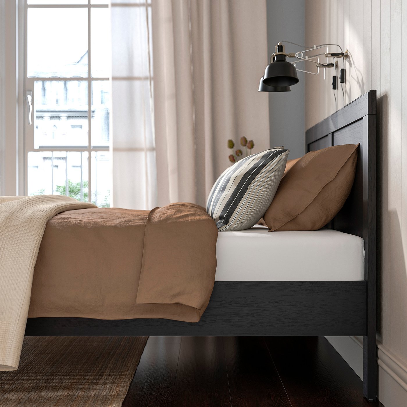 Bedroom scene with FÅGELFJÄLLET bed, dark wood, beige bedding, pillows, bedside lamp, and large window with curtains.