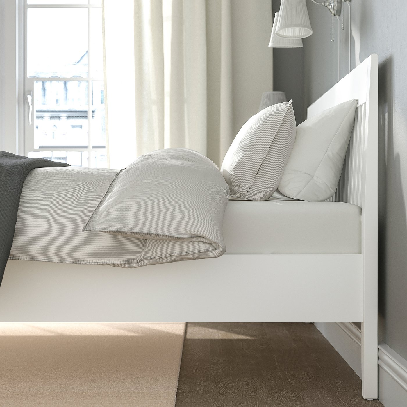 Tidy bedroom corner with white bed frame, lined bedding, curtains, bright window, and wall lamp.