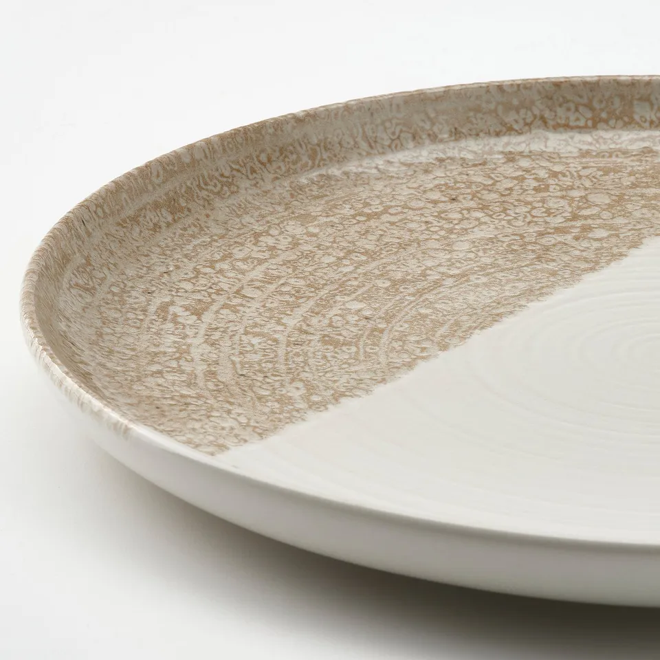 Close-up of a white and tan speckled plates edge, showing its smooth, meticulously crafted surface.