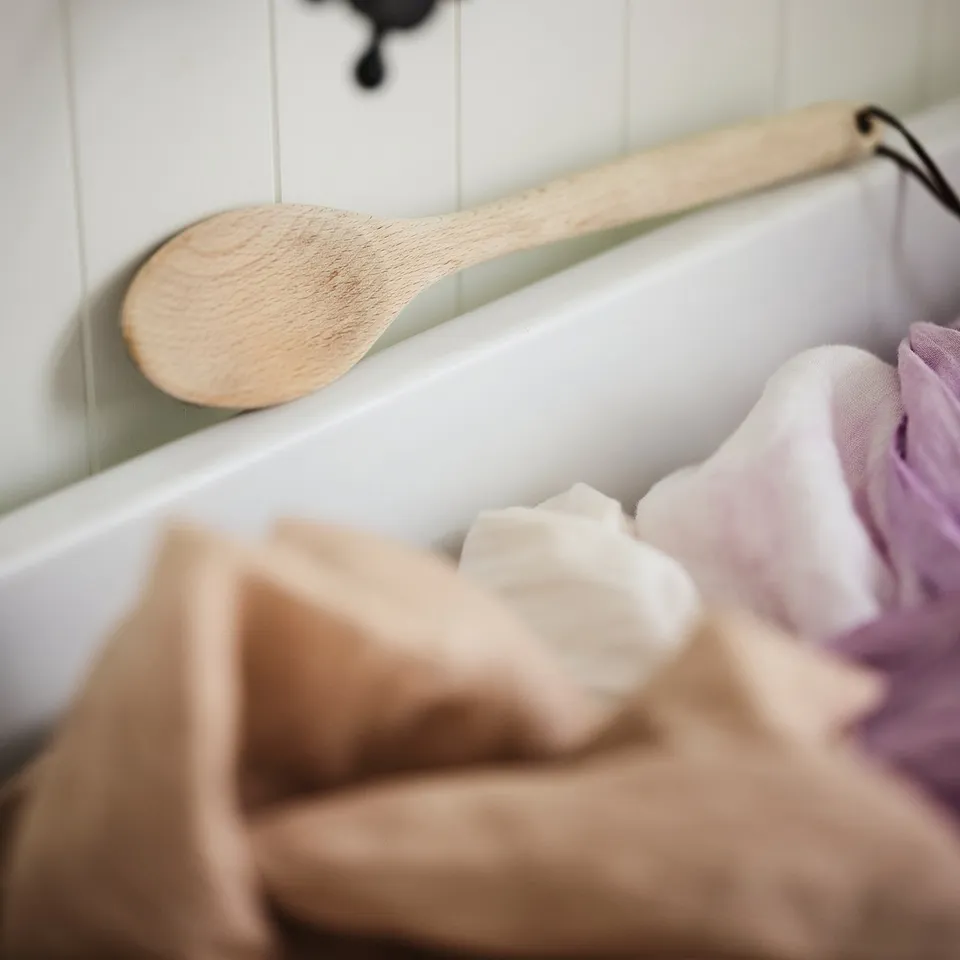 Black sink tap with wooden spoon leaning against white bathtub filled with bars of soap.