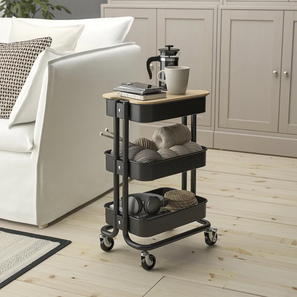 The RÅSKOG trolley, small, black, steel, with wooden top, holds various items, fitting under furniture.