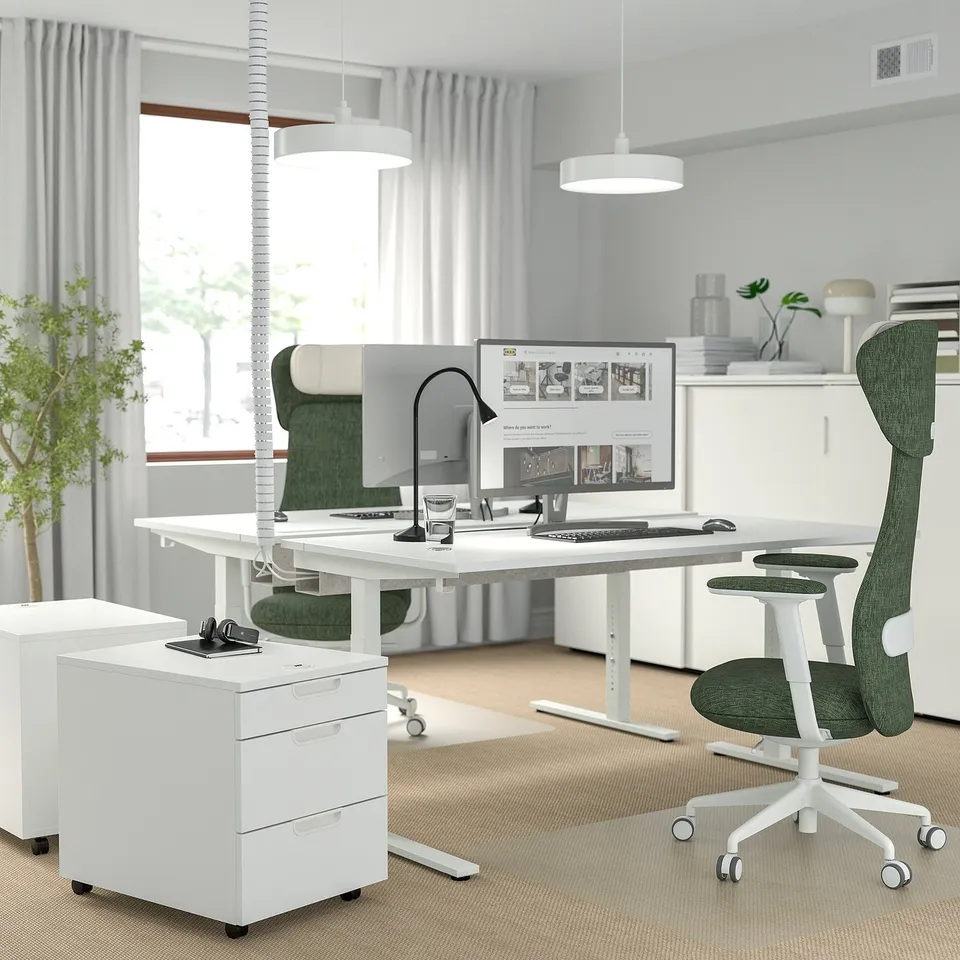 Modern home office with MITTZON white desk, green chair, and sleek design. Computer, lamp, and filing cabinet nearby. Bright and spacious layout.
