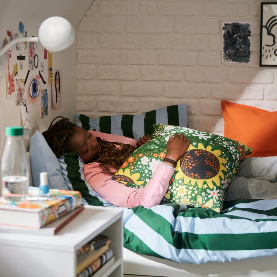 Two kids sleeping on striped bed, orange pillow, sunflower decor, books, water bottle.