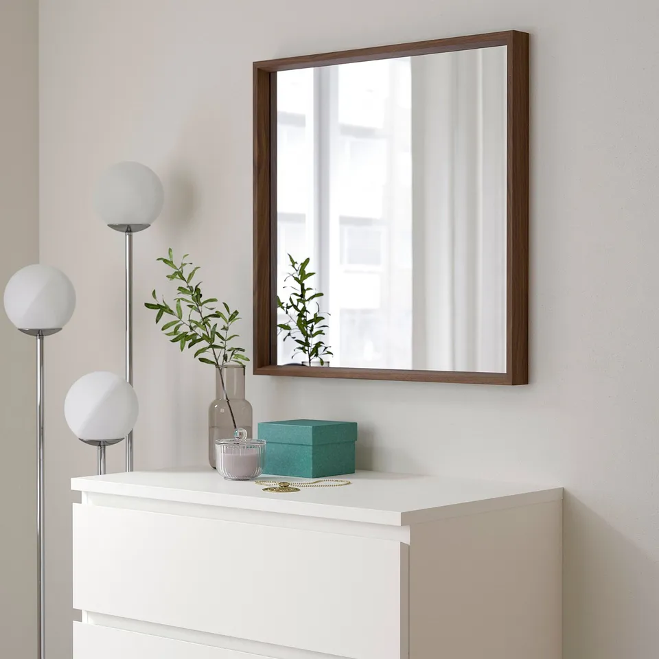 Wall-mounted NISSEDAL mirror with brown frame reflecting window, above white dresser with turquoise box, vase, and lamp.