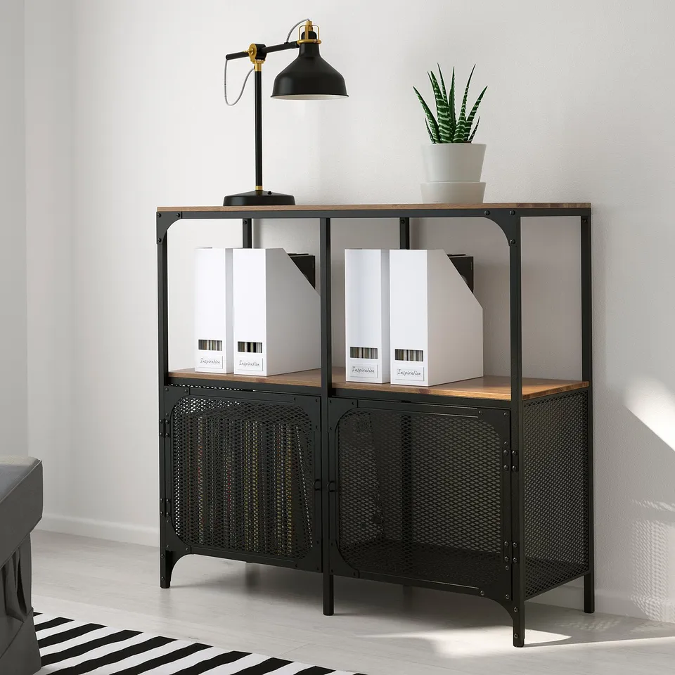 Industrial-style black metal and wood bookshelf with adjustable feet and open back, holding white binders and a black lamp.
