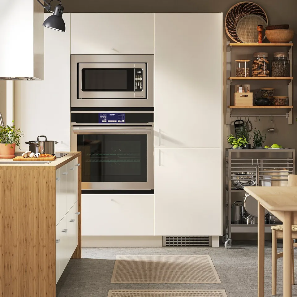 Modern kitchen with silver oven, white cabinets, wooden counter with pots, plant, and open shelves with jars/baskets.