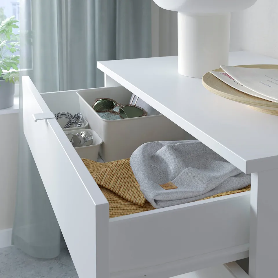 White drawer organiser with compartments holding sunglasses, cords, and a grey garment.