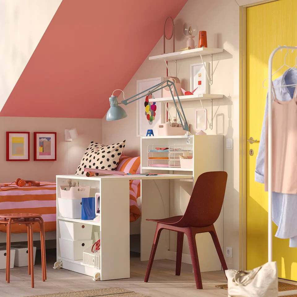 Bright room with white BILLY desk, chair, yellow door, bed, lamp, & colourful frames.