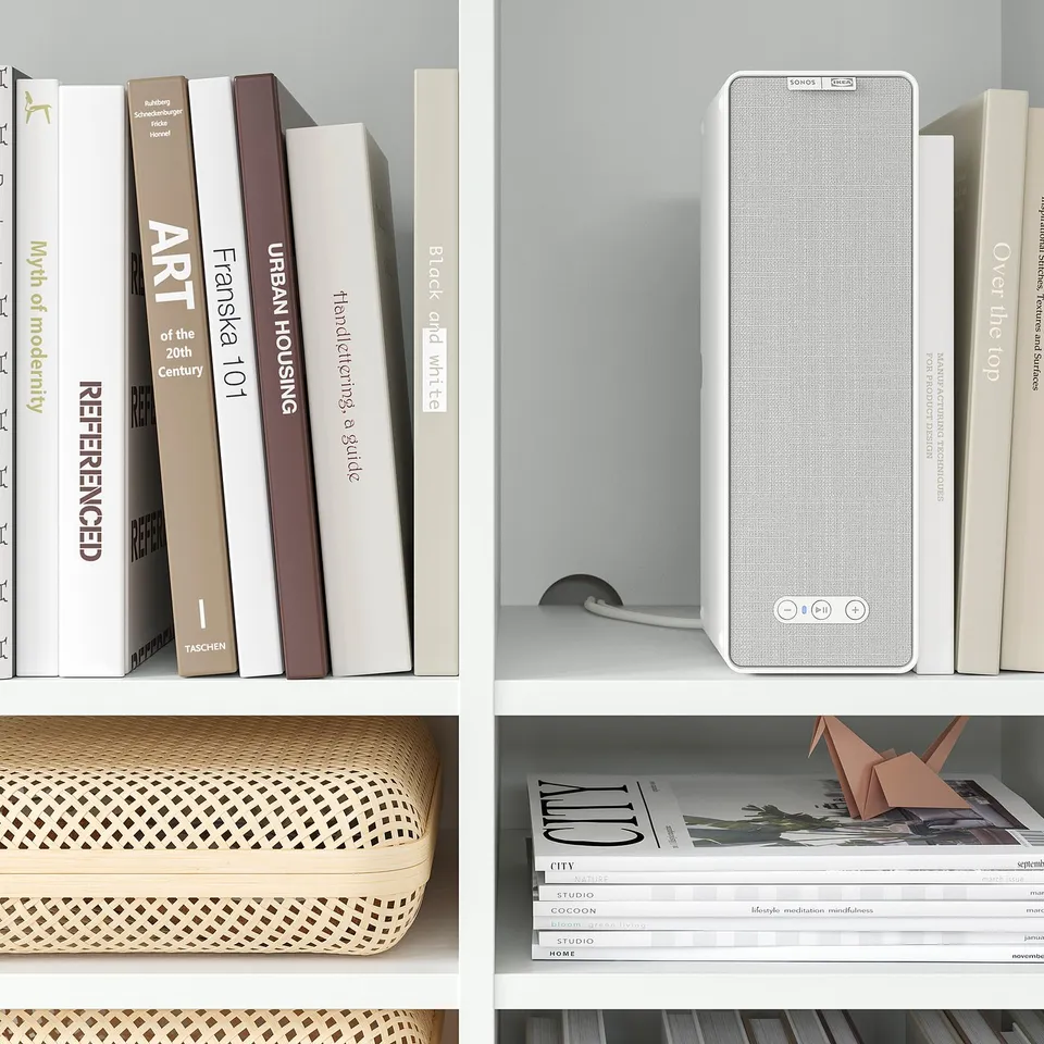 White bookshelf with various books, magazines, a sonos speaker, and decorative items; minimalist design.