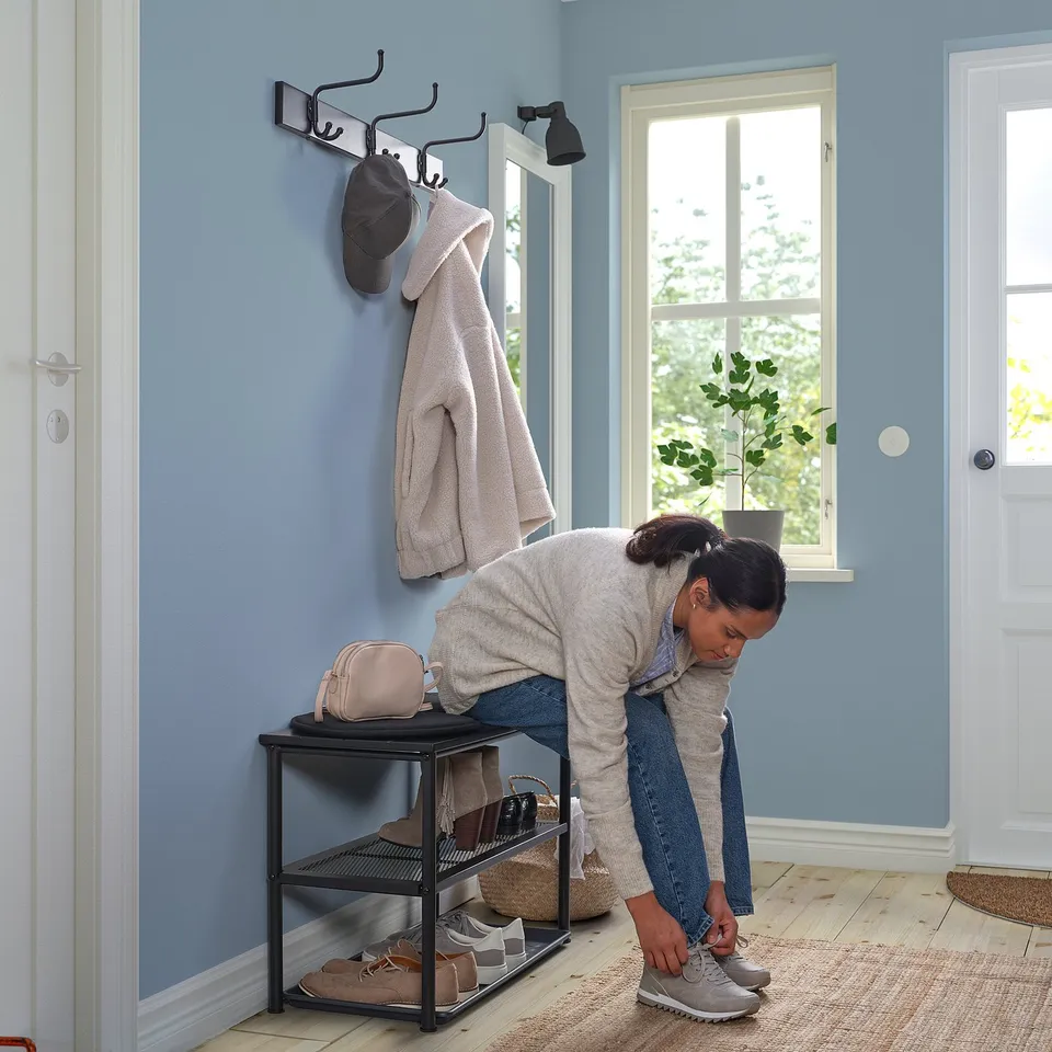 Person tying shoes near organised entryway with hooks, bench, and shelves.