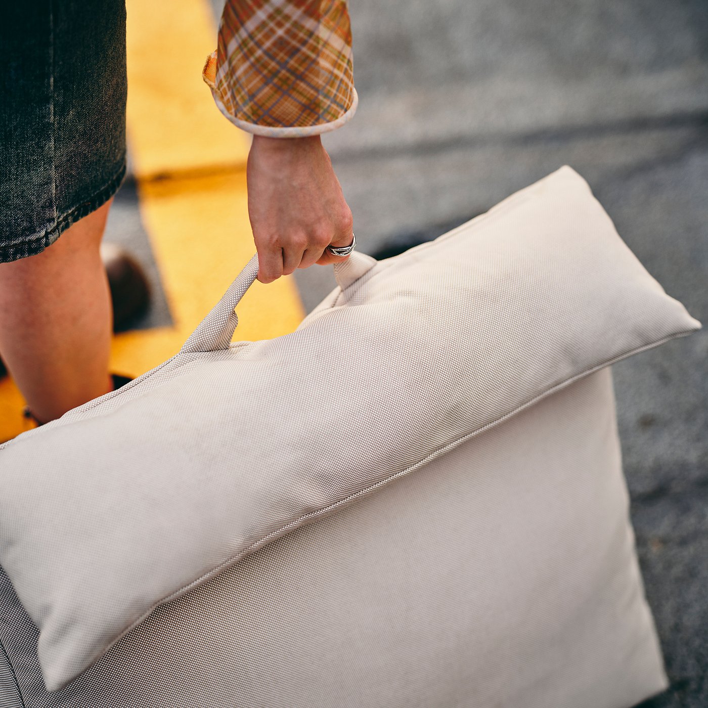 Person holding a large, soft pillow with a textured beige cover and handles, for comfortable seating.