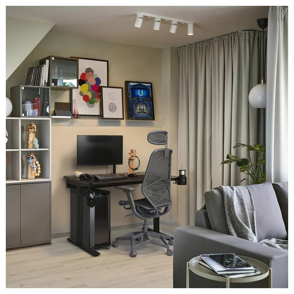 Modern home office with adjustable desk, ergonomic chair, sofa, track lighting, decor, and plants.