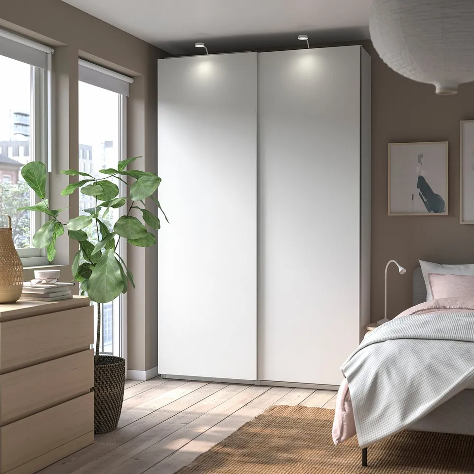 Modern bedroom with white PAX wardrobe, wooden floor, bed, and large plant.