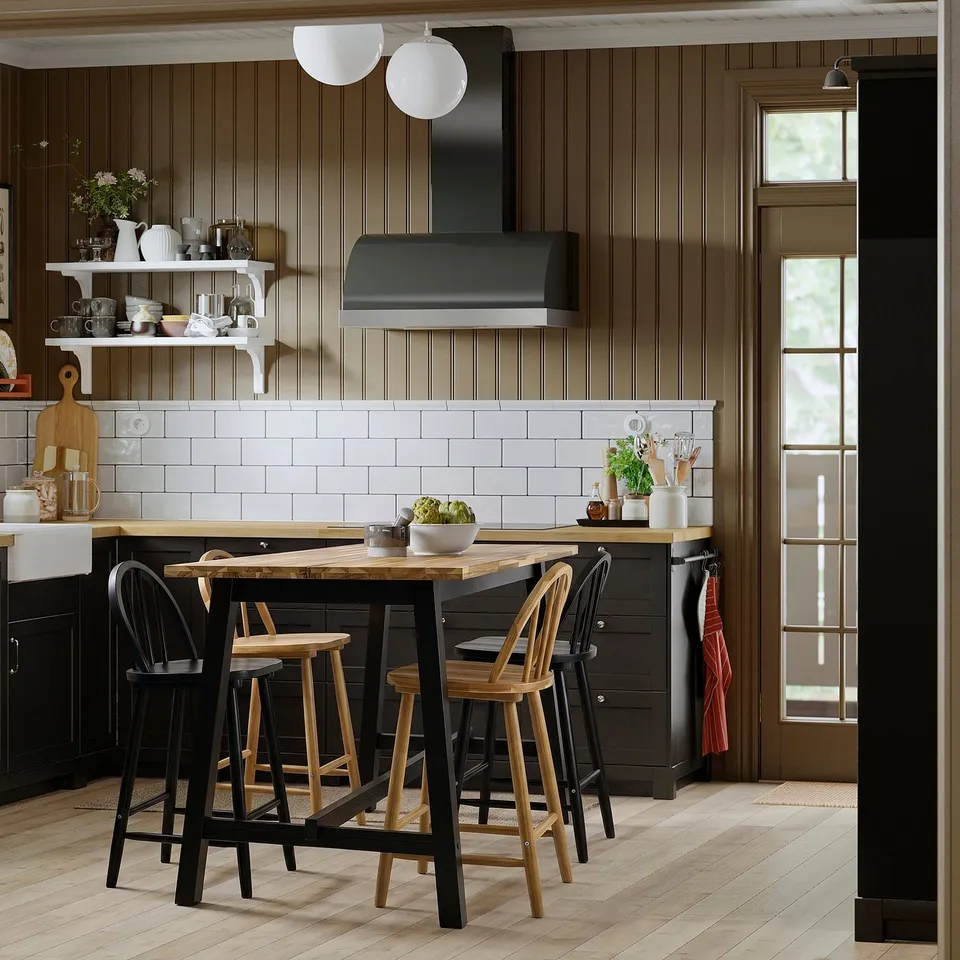 Modern kitchen with SKOGSTA table, black metal, 3 chairs, white backsplash, stainless hood.