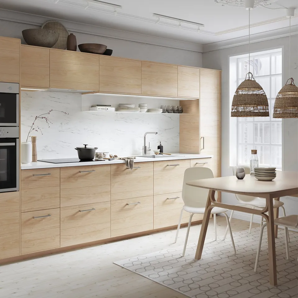 Modern kitchen with light wooden cabinets, marble backsplash, hanging lights, and dining table with chairs.