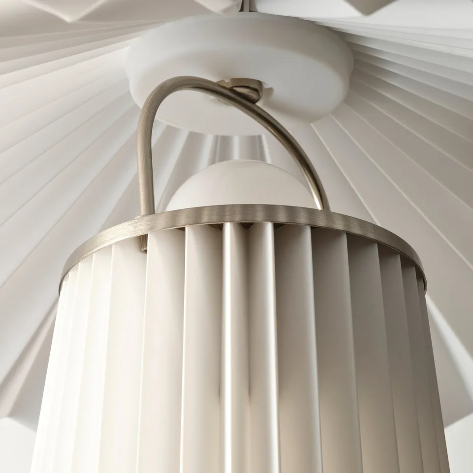 A modern lamp with a pleated shade and sleek metal arm, designed to offer soft, ambient light.
