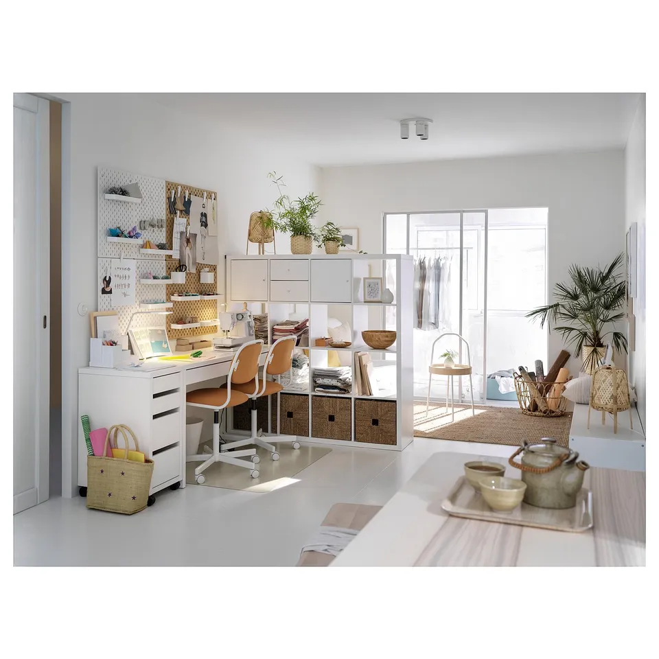 Modern home office with white MICKE desk, chair, and shelves. Wicker baskets, plants, and organised workspace with a pegboard.