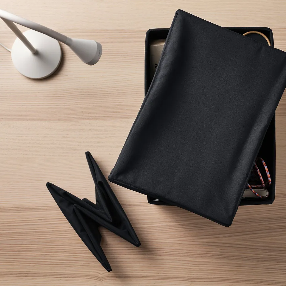 Black fabric lid on wooden surface, partially covering box with visible cables, demonstrating its use to protect contents from dirt and dust.