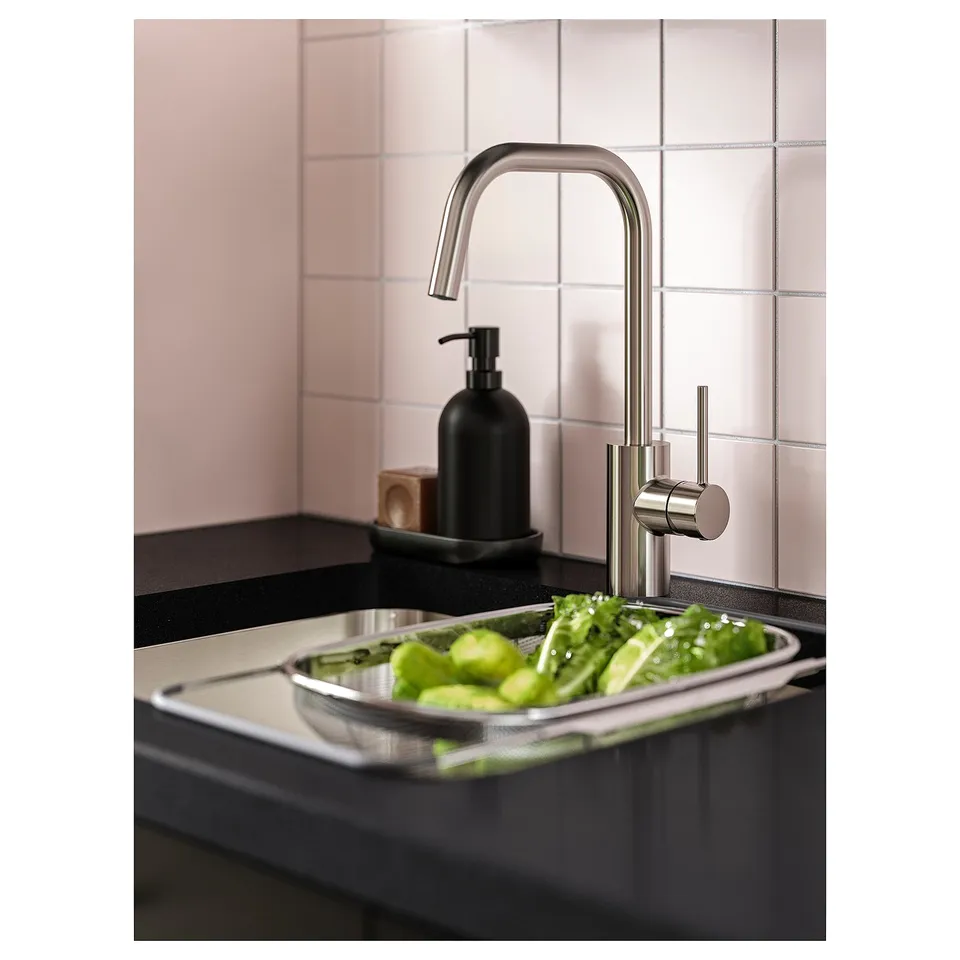 Modern kitchen with stainless steel tap, black soap dispenser, and sink containing green vegetables.