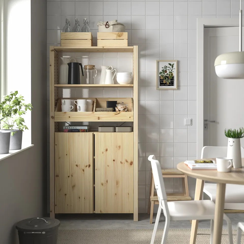 Modern kitchen with wooden IVAR shelf unit displaying cups, jars, and books; light wood, clean lines, and minimalist design.