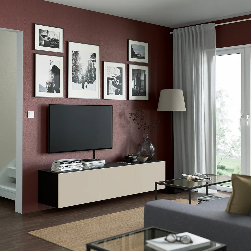 Modern living room with black/white BESTÅ tv bench, maroon wall, grey sofa, large tv, and green view.