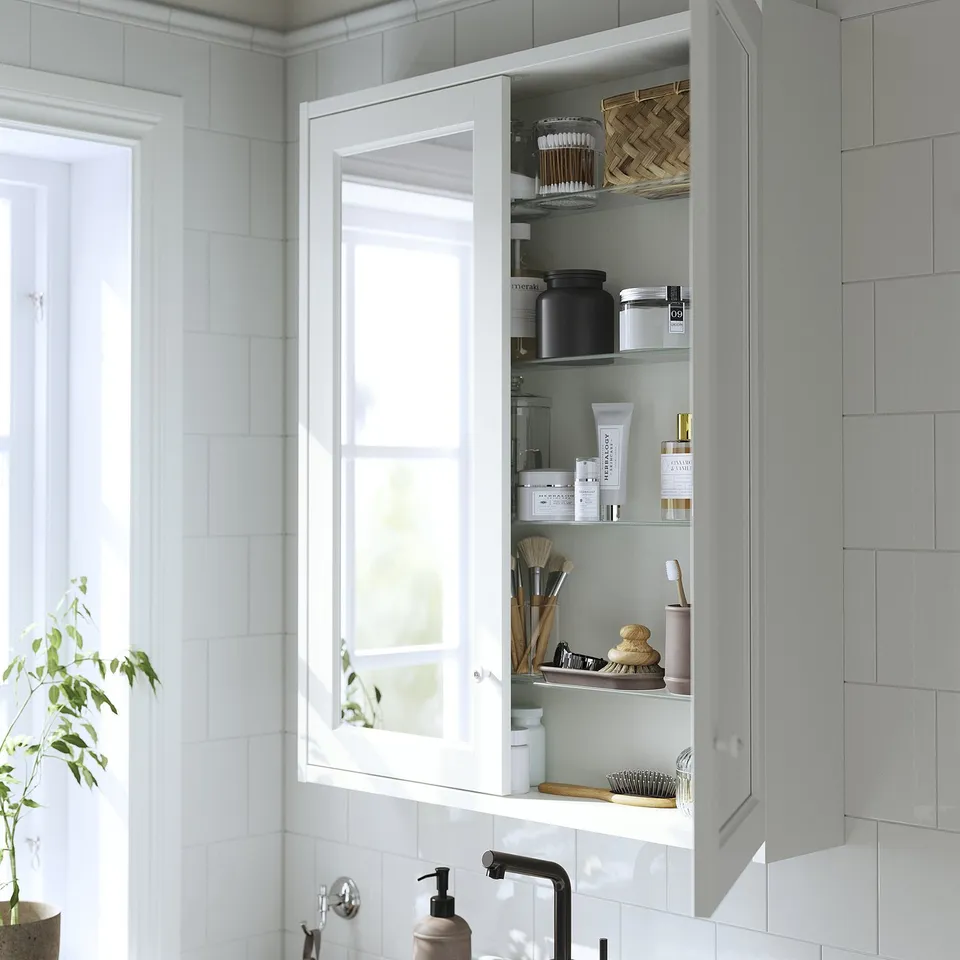 White cabinet with mirror doors, wall-mounted, storing toiletries, neatly organised on shelves.