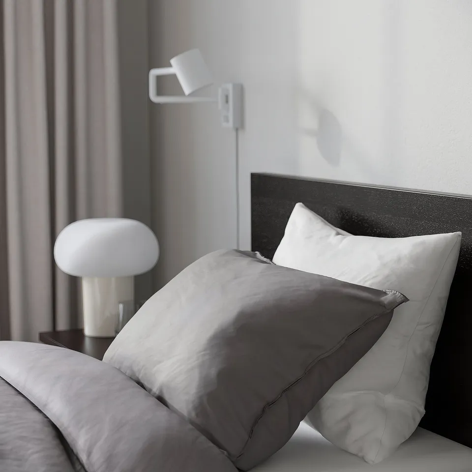 Modern bedroom with grey bedding, white lamp, and dark wood headboard. Adjustable bed with high back for reading support.